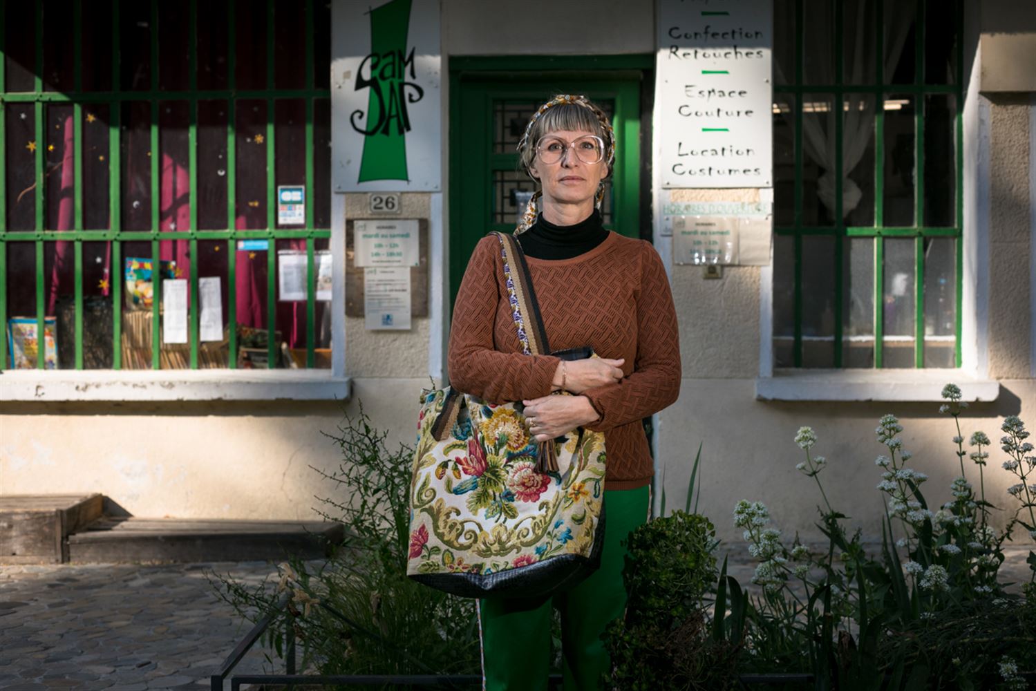 Sarah se tient debout devant une friperie, elle porte un sac kitsch, le soleil du matin dessine un jeu de lumière dorée