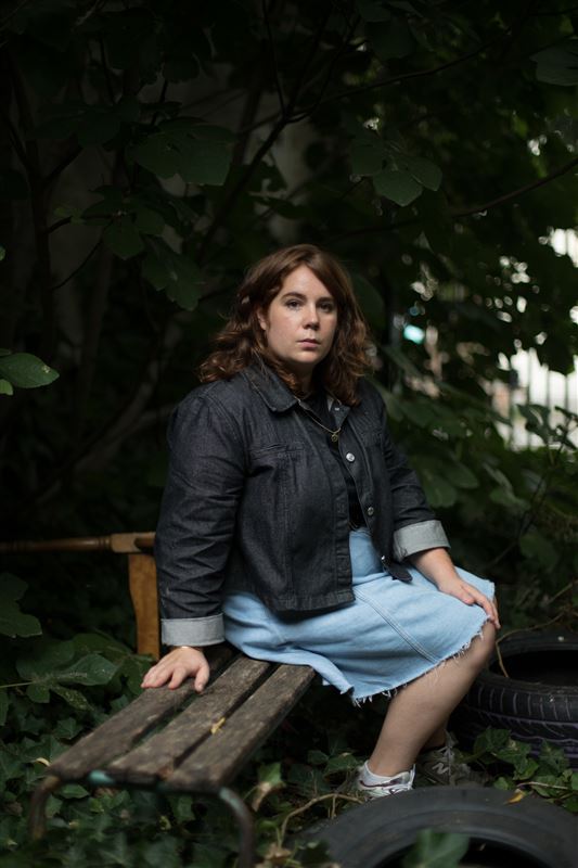 Marie à Arles pose sur une banc vermoulu, au milieu d'orties et de vieux pneus.