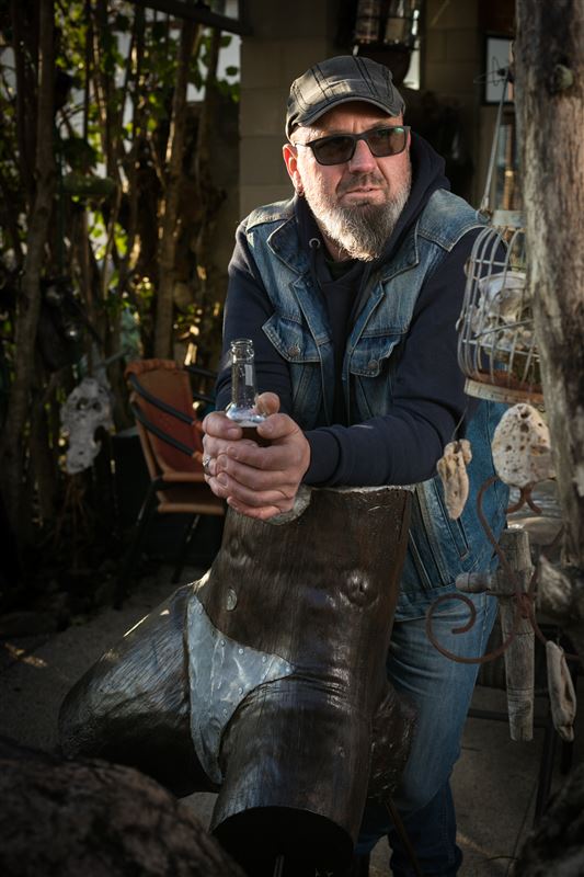 Steph, sculpteur, dessinateur, musicien, repose avec nonchalance sur une sculpture une bière à la main.